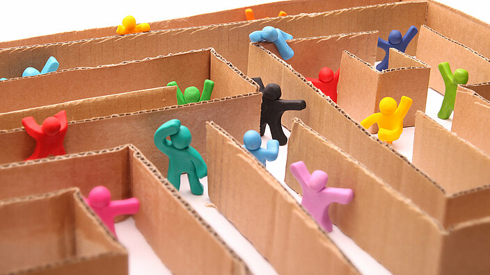 Diverse Knetgummifiguren versuchen einen Ausweg aus einem Labyrinth zu finden.